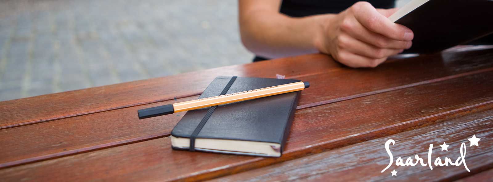 Notizblock mit Stift, Frau liest ein Buch im Freien